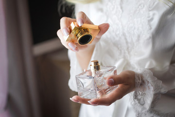 Close up shoot of a luxury fragrant perfume flacon in manicured hands of elegant bride wearing...