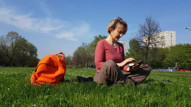 Adult Woman sitting on green grass with mobile phone