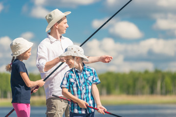 The brother and sister with the father on fishing with fishing rods a summer day