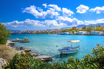 Small natural harbor with anchored fishing boats with the beautiful town of Agios Nikolaos at the...