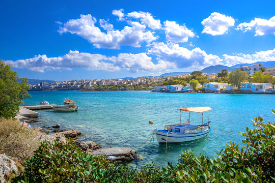 Small natural harbor with anchored fishing boats with the beautiful town of Agios Nikolaos at the background, Crete, Greece.