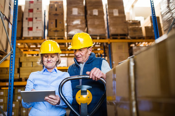 Senior woman manager and man worker with tablet working in a warehouse.