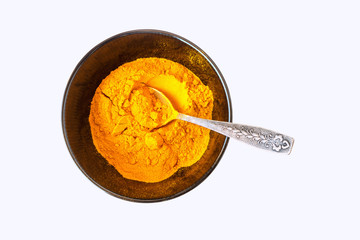 Turmeric powder (Curcuma) in a black bowl with a teaspoon  on white background.  Empty space for text or inscription.