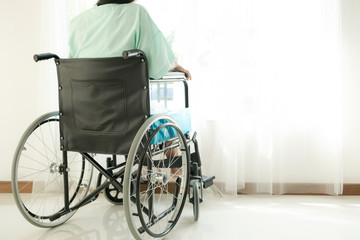 Fototapeta premium Young woman in hospital wheel chair. Looking at window. Beautiful chinese woman. Medical, health insurance concept.