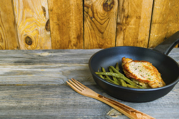 fried chicken fillet and asparagus in a frying pan on an old wooden background