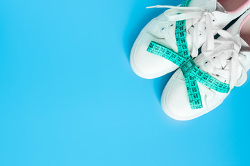 Sneakers are tied with measuring tape in a bow on a blue background. The concept of an active lifestyle, flat lay. Promotion of walking and a bonus weight loss.Top view.Copy space.