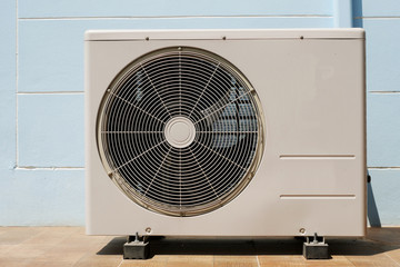 Air Conditioner Condenser Unit at a Blue Color Painted Concrete Wall 