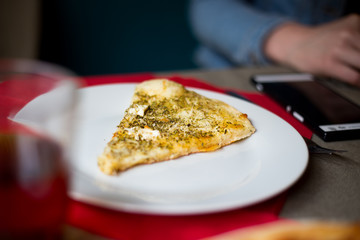 A slice of freshly baked italian four cheese pizza on a white plate at a restaurant