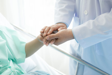 Doctor with patient. Routine health check and holding hands. Male medical doctor with young chinese woman.