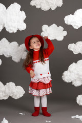 girl playing with clouds, dressed in red sweater, shot in the studio on a gray background