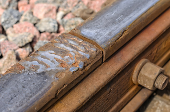 Damaged rusty rail used on working railroad tracks, fragment of the rail with joint and bolt, small gravel in the background, close-up, safety violation
