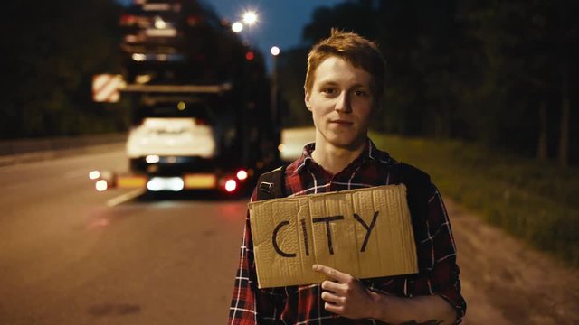 Traveler, young man hitchhiking with sign on the road at night