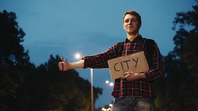 Traveler, young man hitchhiking with sign on the road at night