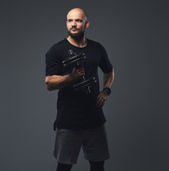 Portrait of a handsome bearded athlete in a black t-shirt, posing dumbbell in a studio.