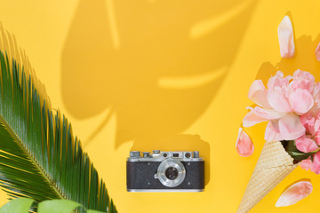 Top view of summer background with Tropical palm tree leaf, vintage photo camera, flowers on a trendy bright yellow background, flat lay