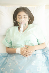 Young patient alone in bed. Sleeping in hospital bed. Oxygen mask on her face. Young beautiful chinese woman.