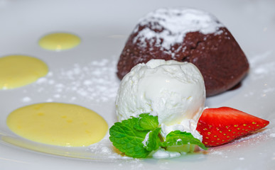 Теплый шоколадный фондант с шариком мороженого и клубникой на белой тарелке.