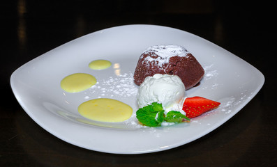 Теплый шоколадный фондант с шариком мороженого и клубникой на белой тарелке.