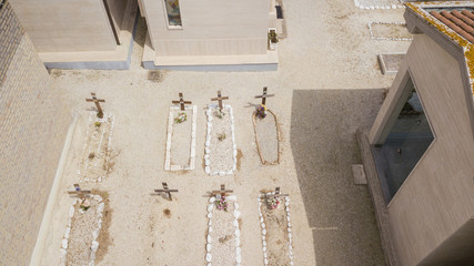 Aerial view of a small municipal cemetery. The tombs are placed both on the ground and in small concrete mausoleums. There are many flowers in memory of the deceased loved ones.