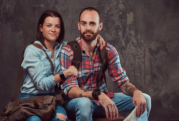 Happy couple of tourists with backpack and map, cuddling while sitting on a bench in a studio.
