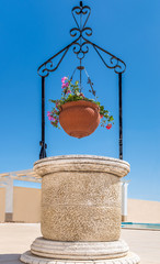 ornamental stone patio well and hanging terra cotta flower basket with geraniums against a blue sky
