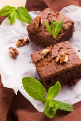 Brownie sweet chocolate dessert with walnuts and meant leaves on white paper with copy space on pastel beige background.