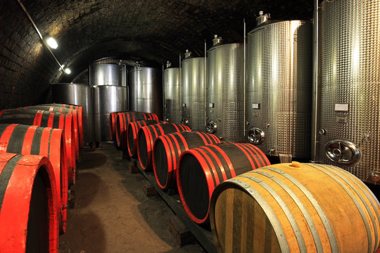 Wine barrels in wine cellar with modern fermentor tanks