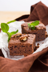 Brownie sweet chocolate dessert with walnuts and meant leaves on white paper with copy space on pastel beige background.