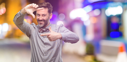 Middle age man, with beard and bow tie confident and happy showing hands to camera, composing and framing gesture at night club