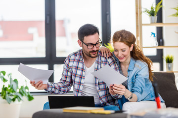 Obraz premium Young couple moving in new home. Sitting and relaxing after unpacking. Searching home decorating ideas on laptop.