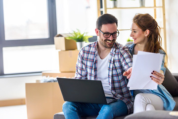 Young couple moving in new home. Sitting and relaxing after unpacking. Searching home decorating ideas on laptop.