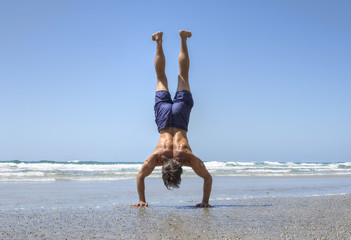Fototapeta na wymiar Muscular man doing handstand on beach