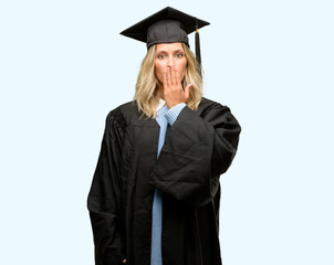 Young graduate woman covers mouth in shock, looks shy, expressing silence and mistake concepts, scared