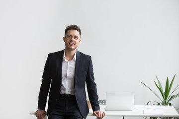 Smiling company CEO leaning back at office table posing near desk looking at camera satisfied with...