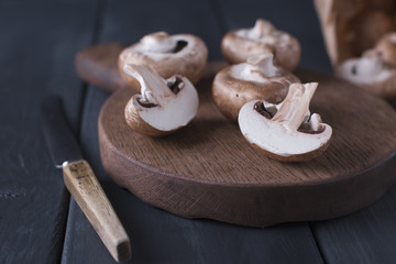 Mushrooms champignons on a wooden board and knife. Ingredients for cooking dinner. Dark photo. Text