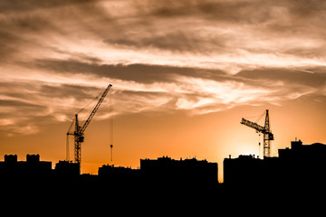the silhouettes of two tower cranes and houses during sunset, sunset with an orange sky in the city