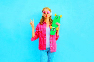 Fashion woman with a skateboard listens to music in wireless headphones