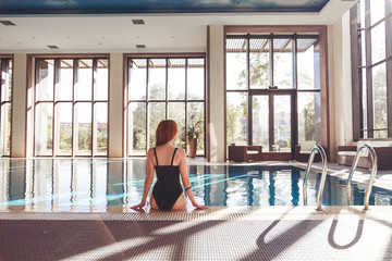 Enjoying vacation. Back view of slim young woman drinking cocktail in swimming pool.