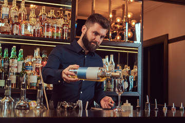Stylish brutal barman in a black shirt makes a cocktail at bar counter background.