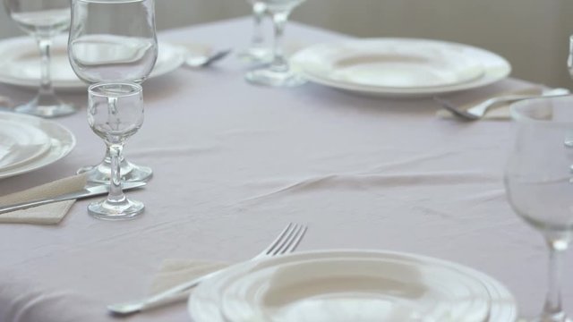 Fine dining table setting in restaurant with plates cutlery and stemware. Closeup pan shot.
