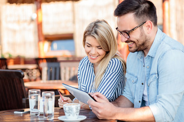 Happy young couple browsing online shop on a tablet, sitting in a cafe