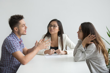 Young nervous millennial couple fighting sitting in counselor office arguing, husband explaining opinion to wife ignoring his words, trying to save marriage, receiving help from relationship advisor
