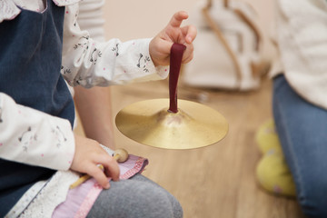 A girl toddler plays cymbals in a Montessori music class