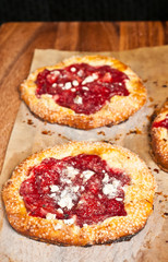 Top view of two freshly baked, homemade, rustic, strawberry ricotta tarts on parchment paper cooling on a wood cutting board