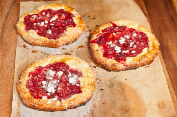 Top view of three freshly baked, homemade, rustic, strawberry ricotta tarts on parchment paper cooling on a wood cutting board