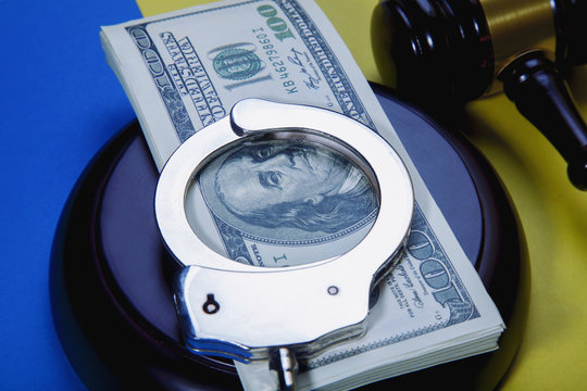 Dollar banknotes,  handcuffs  and judge's gavel on the background of yellow and blue colors as symbol of corruption in the judicial system in Ukraine