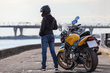 Fototapeta na wymiar Rear view at female biker in crash helmet standing next to bikes on street embankment, full-length