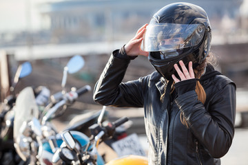 Obraz premium Motocyklista rasy kaukaskiej kobieta ustawia swój pełny kask, portret na tle rowerów, kopia przestrzeń