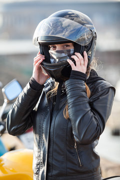 Young woman motorcyclist put on crash helmet for riding bike on urban road