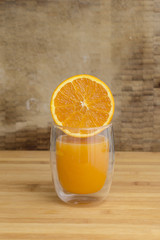 Half orange juicy fruit on a transparent drinking glass isolated on a brown wooden background